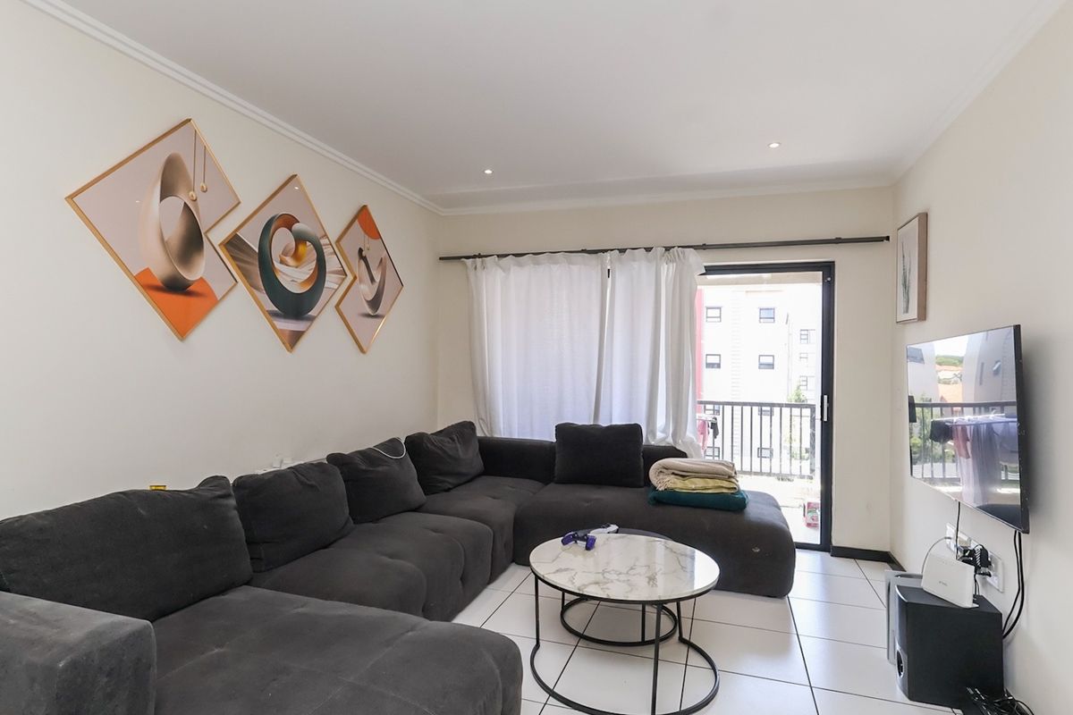A bright and well-maintained living room featuring tiled flooring, recessed lighting, and direct access to a private balcony through a sliding glass door.