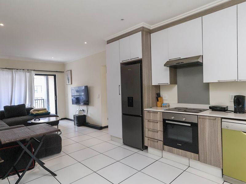Modern open-plan living area featuring a contemporary kitchen with built-in appliances, tiled flooring, and direct access to a balcony.