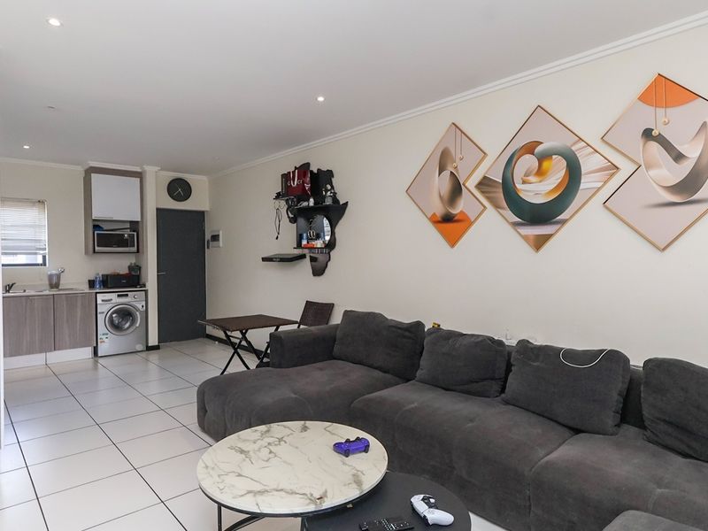 An open-plan living area featuring tiled floors, recessed lighting, and a compact kitchen corner with built-in cabinetry and laundry facilities.