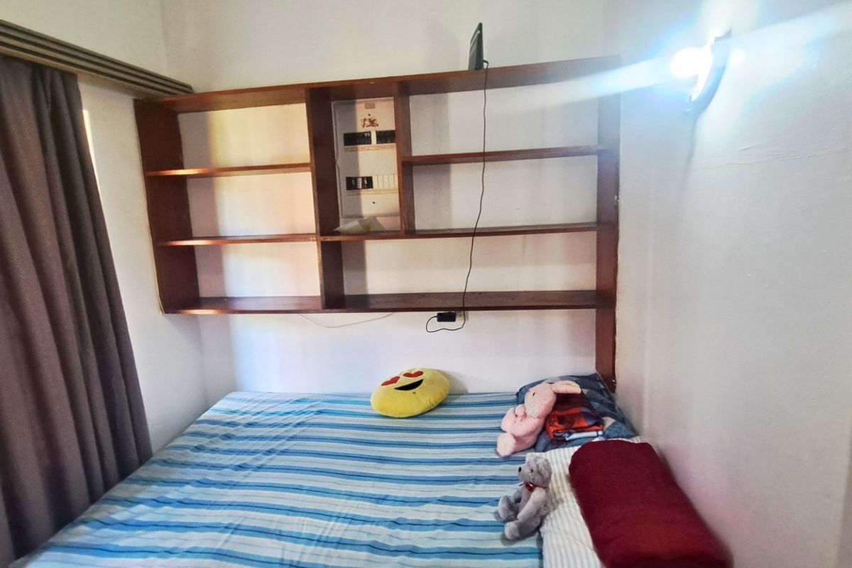 A bedroom featuring a built-in wooden shelving unit with an integrated electrical distribution board and wall-mounted lighting.