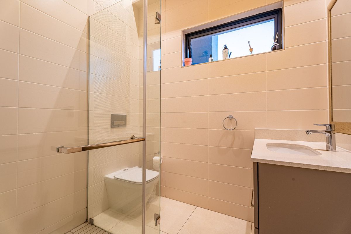 Modern bathroom featuring a glass-enclosed shower, wall-mounted toilet, and a sleek vanity with a stone countertop.