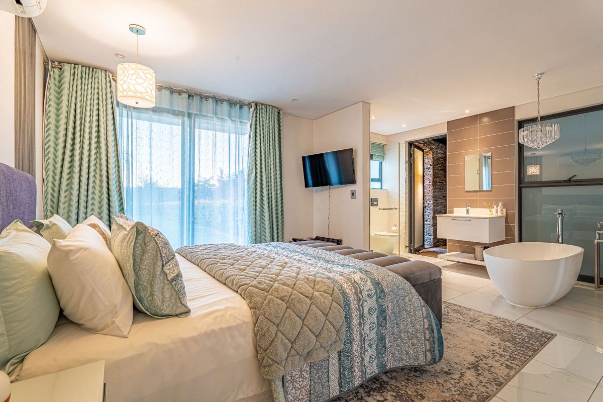 Spacious bedroom featuring an open-plan en-suite bathroom with a freestanding bathtub, modern vanity, and sliding glass doors leading to the exterior.