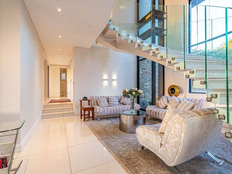 Elegant entrance hall featuring a modern floating staircase with glass balustrades, polished tile flooring, and double-volume windows overlooking a stone feature wall.
