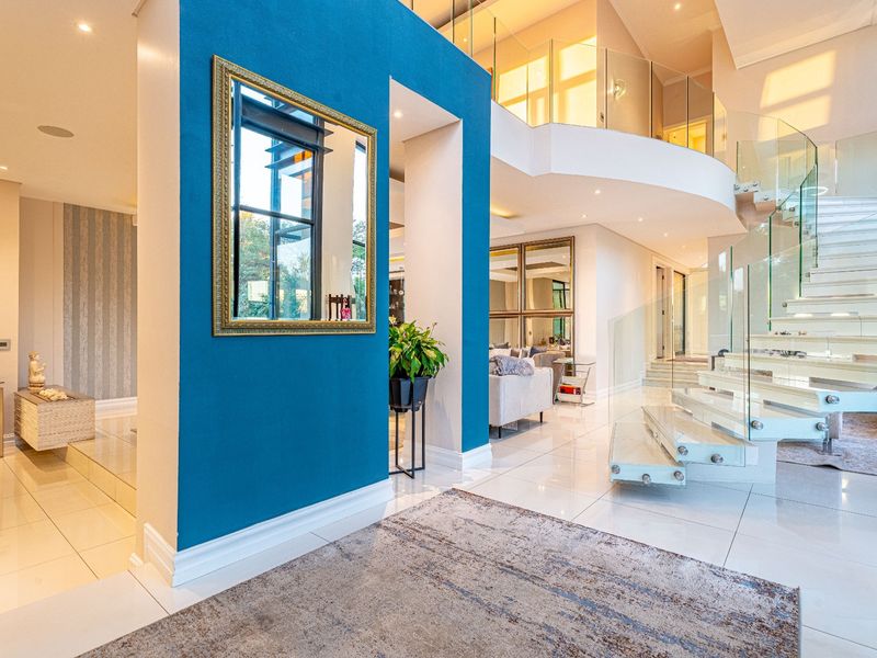 Spacious modern entry hall featuring a striking blue accent wall, polished porcelain floor tiles, and a contemporary floating staircase with glass balustrades.