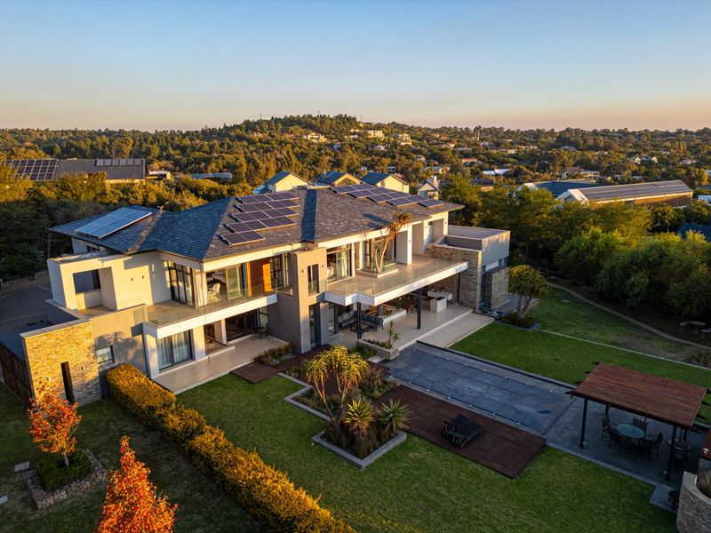 Aerial view of a modern luxury residence featuring extensive solar panel arrays, a swimming pool, landscaped gardens, and spacious covered patio areas.