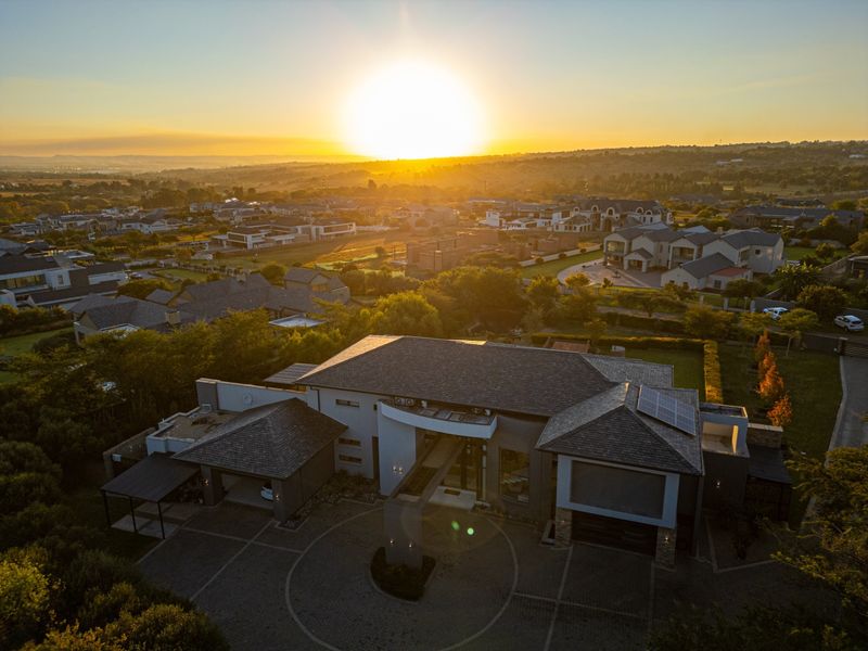 Aerial view of a modern residential property featuring a paved circular driveway, multi-car garage, and solar panels on the roof at sunset.