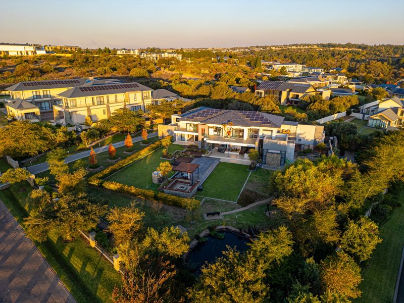 Aerial view of a modern residential property featuring a landscaped garden, a built-in fire pit area, and solar panels installed on the roof.