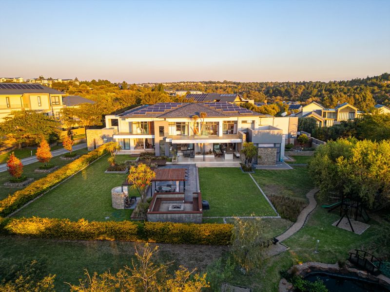 Aerial view of a modern luxury residence featuring a spacious landscaped garden, outdoor entertainment area with fire pit, and solar panel installation.