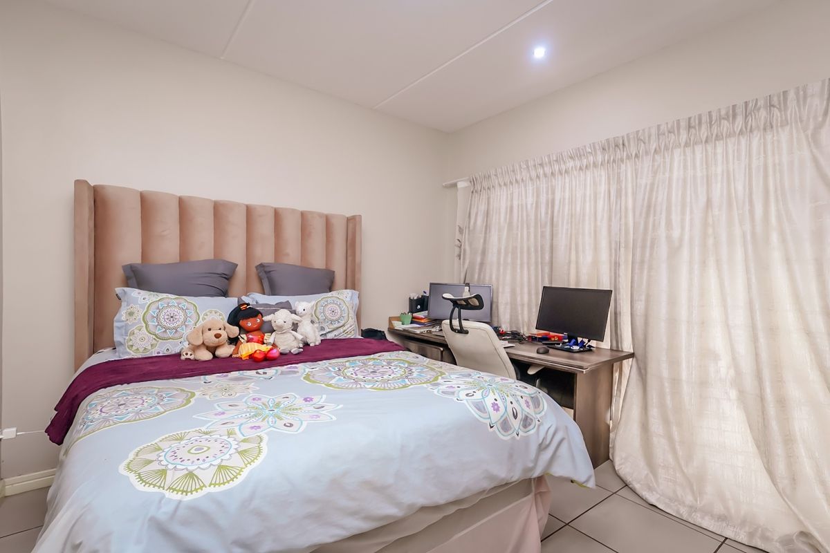 A well-maintained bedroom featuring tiled flooring, neutral wall finishes, and a large window dressed with floor-to-ceiling curtains.