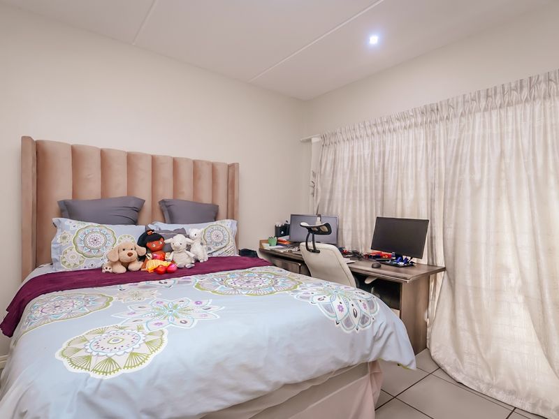 A well-maintained bedroom featuring tiled flooring, neutral wall finishes, and a large window dressed with floor-to-ceiling curtains.