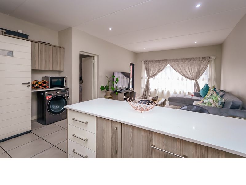 Modern open-plan living area featuring a kitchen island with stone countertop, tiled flooring, and integrated cabinetry, seamlessly connecting to the lounge space.