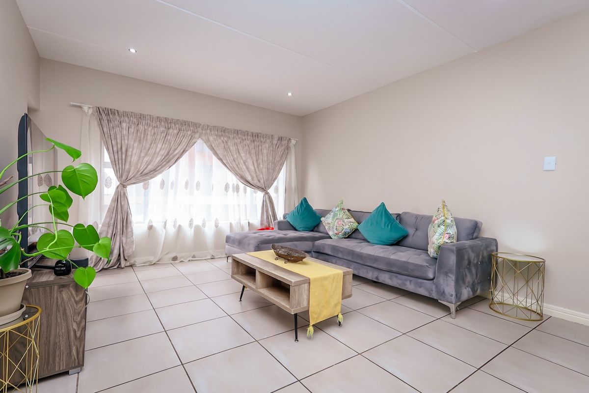 A bright and well-maintained living room featuring neutral tiled flooring and recessed downlighting, providing a clean and comfortable space.
