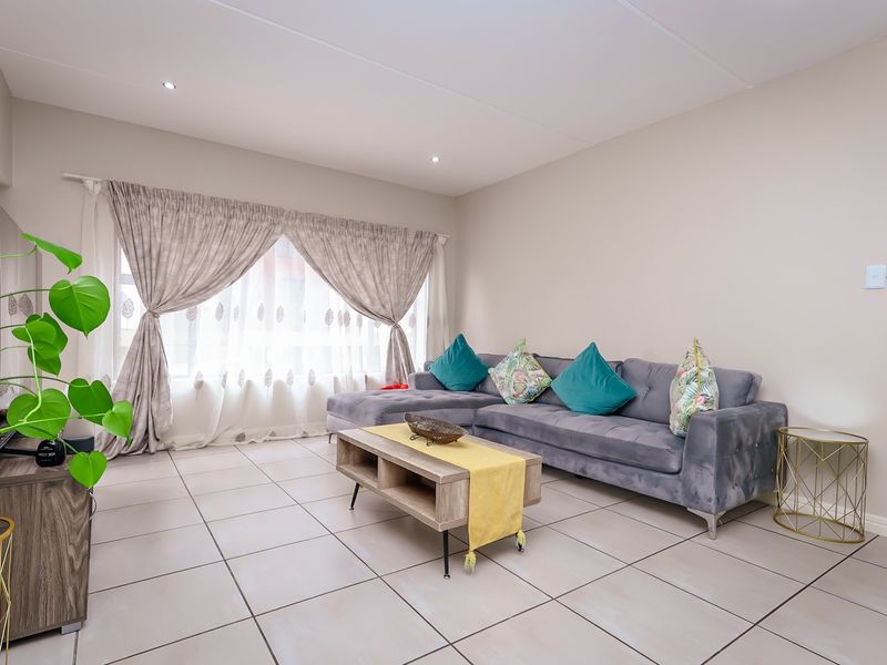 A bright and well-maintained living room featuring neutral tiled flooring and recessed downlighting, providing a clean and comfortable space.