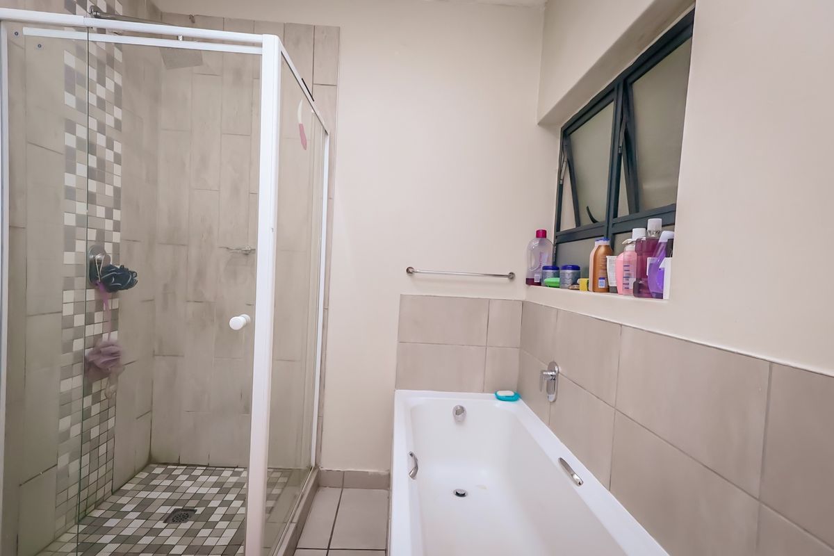 A functional bathroom featuring a separate shower enclosure, a bathtub, and neutral wall and floor tiling with a window for natural light.