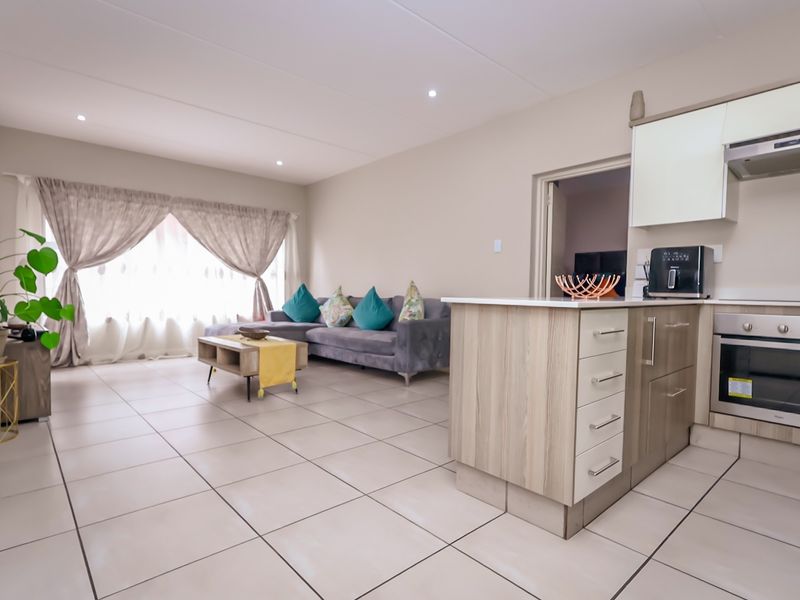 An open-plan living and kitchen area featuring tiled flooring, modern cabinetry, a built-in oven, and an integrated kitchen island.
