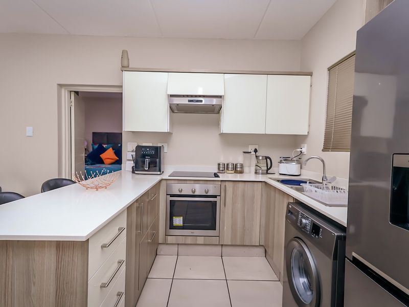 Modern kitchen featuring light wood-grain cabinetry, white quartz countertops, integrated oven and hob, and a convenient breakfast bar for casual dining.