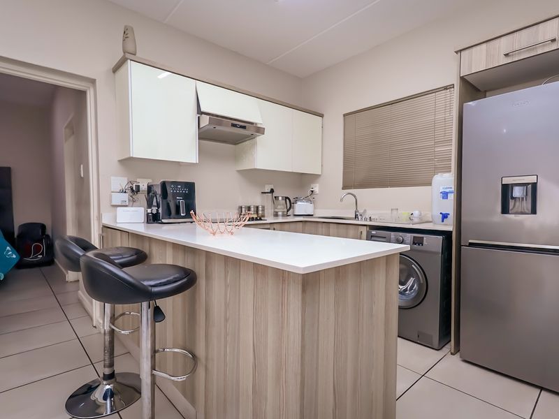 Modern kitchen featuring light wood-finish cabinetry, a breakfast bar, integrated sink, and tiled flooring, offering a functional and contemporary cooking space.