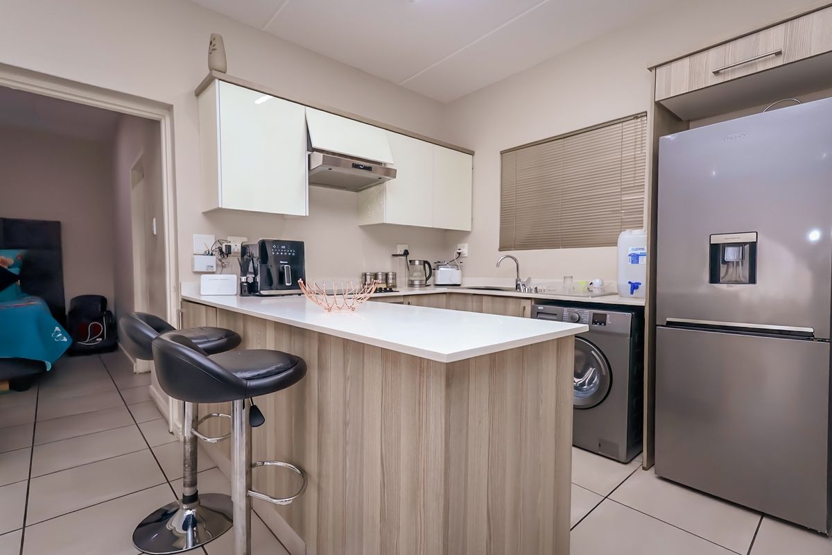 Modern kitchen featuring light wood-finish cabinetry, a breakfast bar, integrated sink, and tiled flooring, offering a functional and contemporary cooking space.