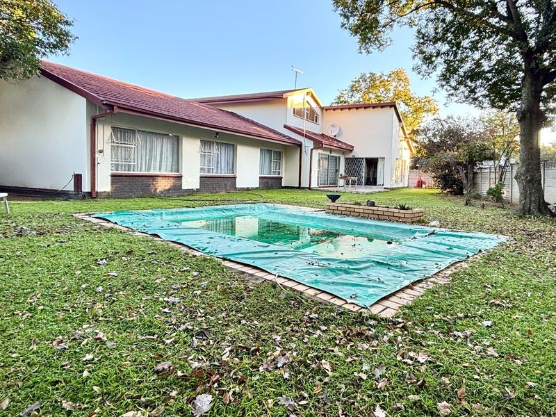 Rear view of the property featuring a spacious garden, a swimming pool with a cover, and a brick boundary wall.