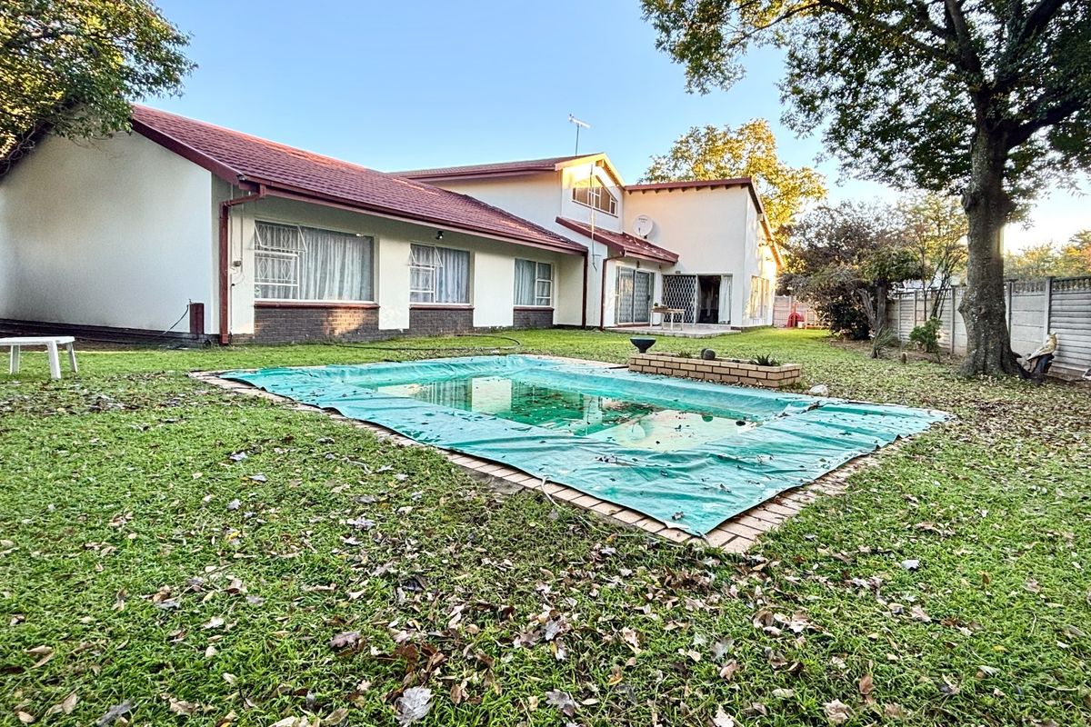 Rear view of the property featuring a spacious garden, a swimming pool with a cover, and a brick boundary wall.