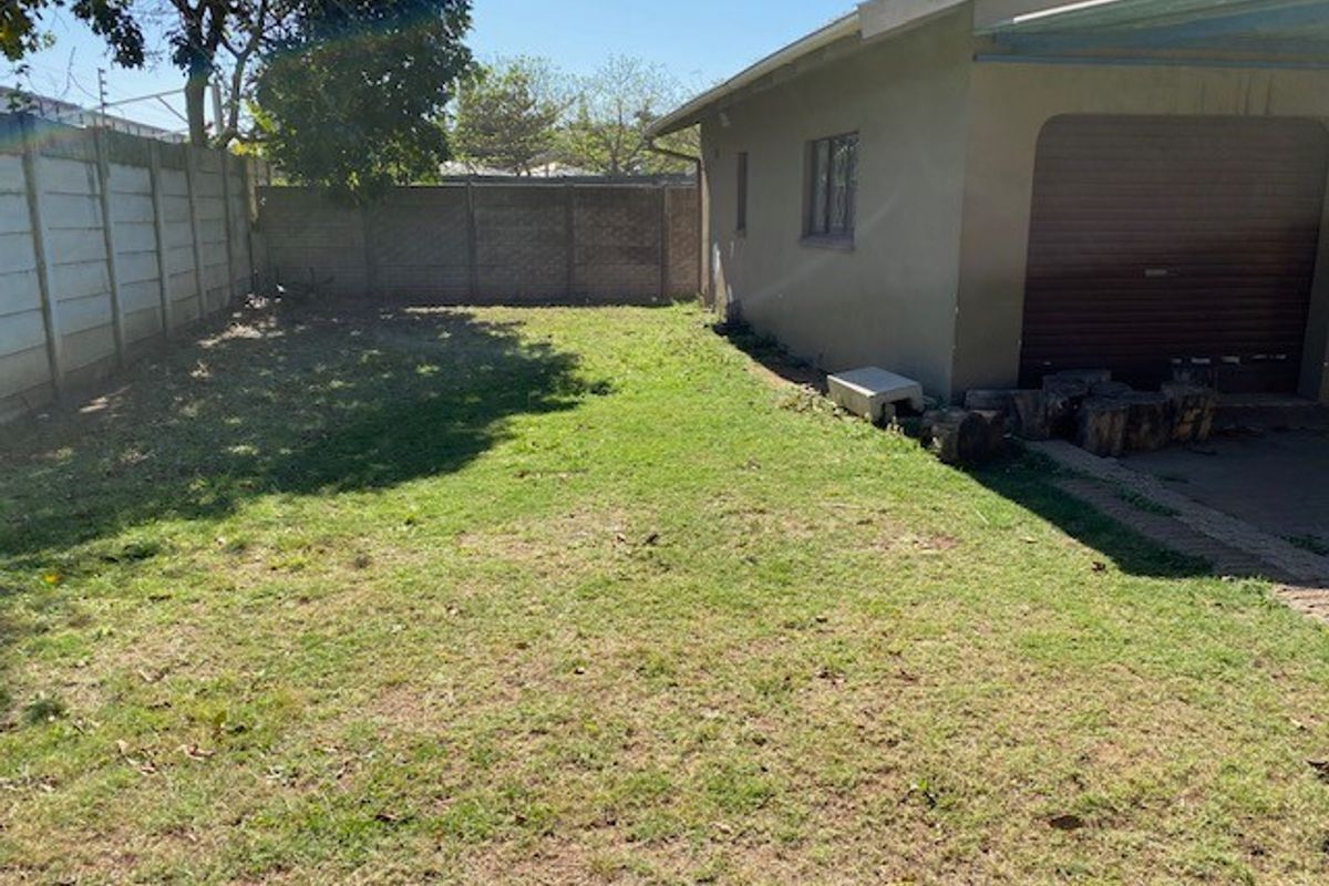 A view of the rear yard featuring a lawn area, enclosed by a precast concrete boundary wall, adjacent to the garage structure.