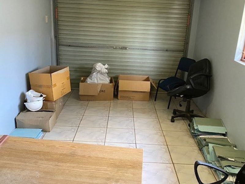 A functional garage space featuring a roller shutter door and tiled flooring, currently used for storage.