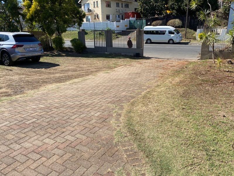 Front view of the property featuring a paved driveway, metal entrance gate, and boundary wall with electric fencing.