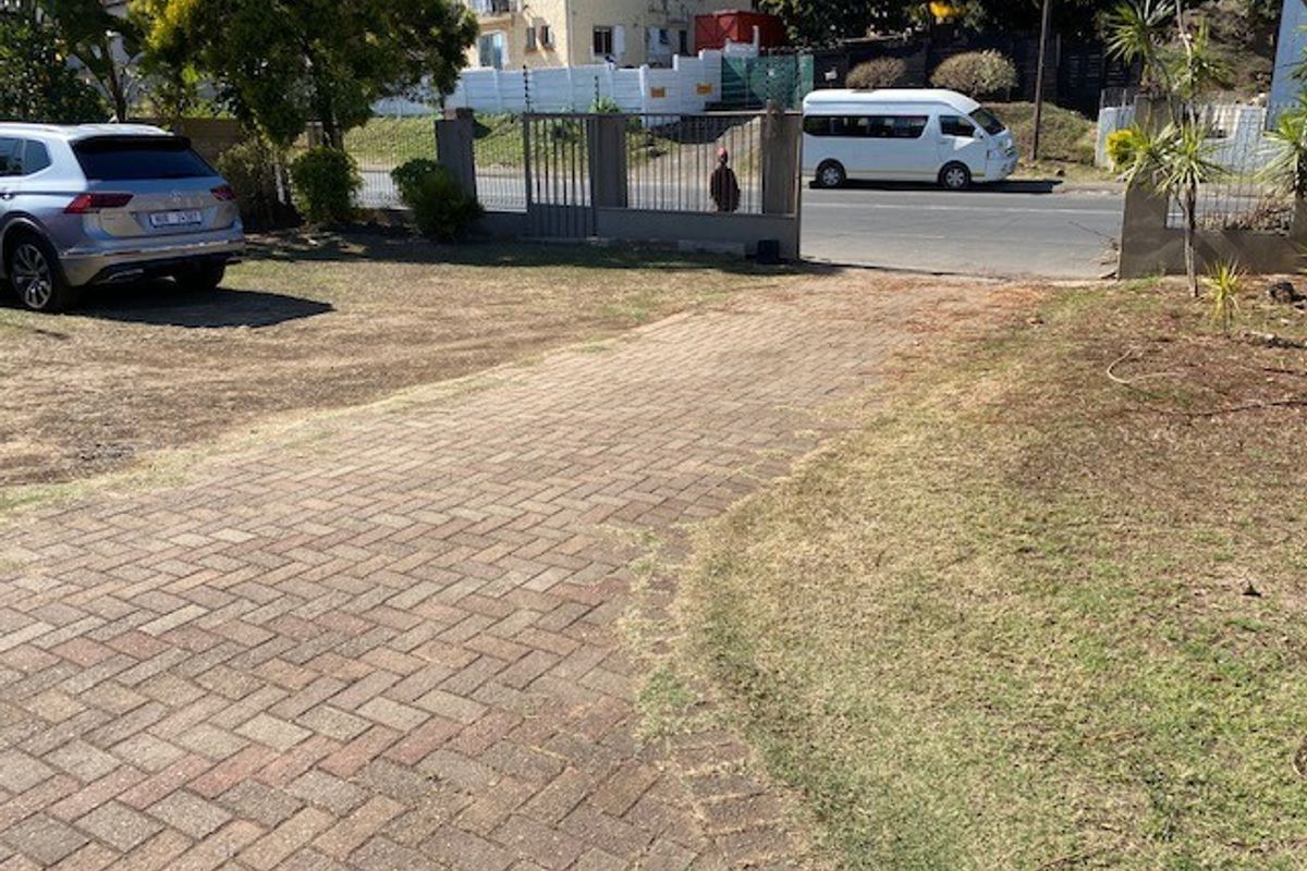 Front view of the property featuring a paved driveway, metal entrance gate, and boundary wall with electric fencing.