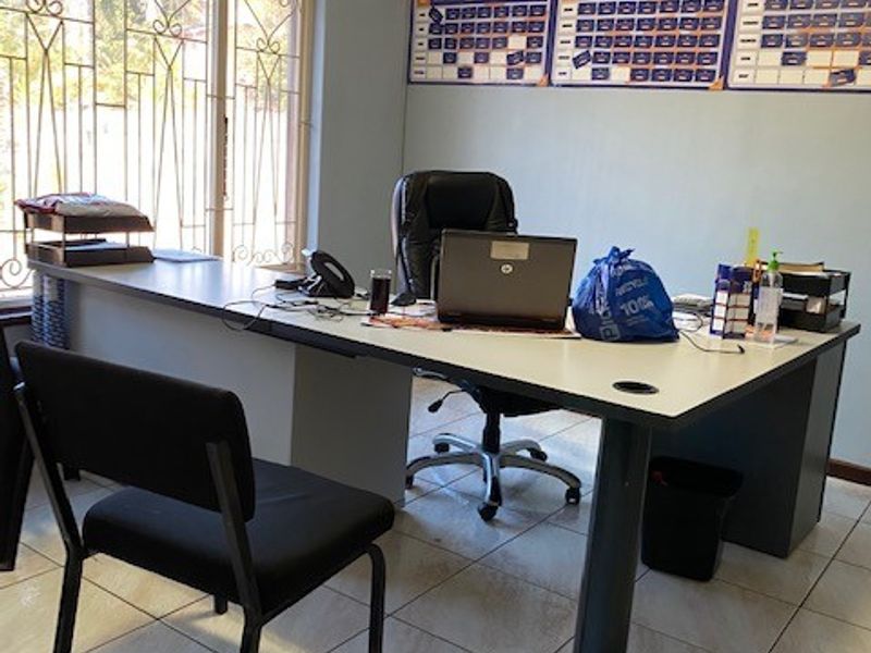 A functional office space featuring tiled flooring, a wall-mounted air conditioning unit, and large windows secured with decorative metal bars.