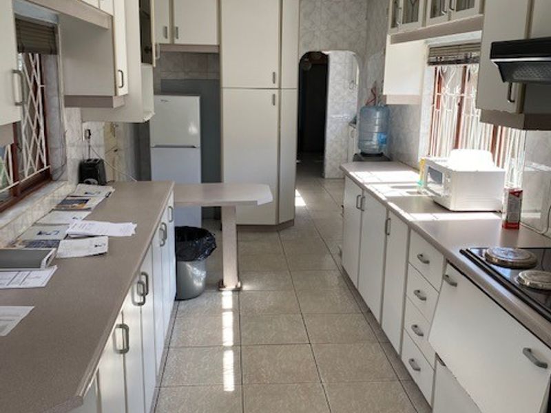 A functional galley-style kitchen featuring white built-in cabinetry, laminate countertops, ceramic tile flooring, and an integrated electric hob with an extractor fan.