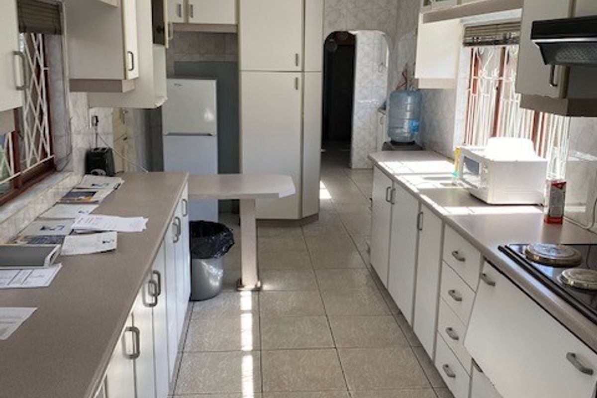 A functional galley-style kitchen featuring white built-in cabinetry, laminate countertops, ceramic tile flooring, and an integrated electric hob with an extractor fan.