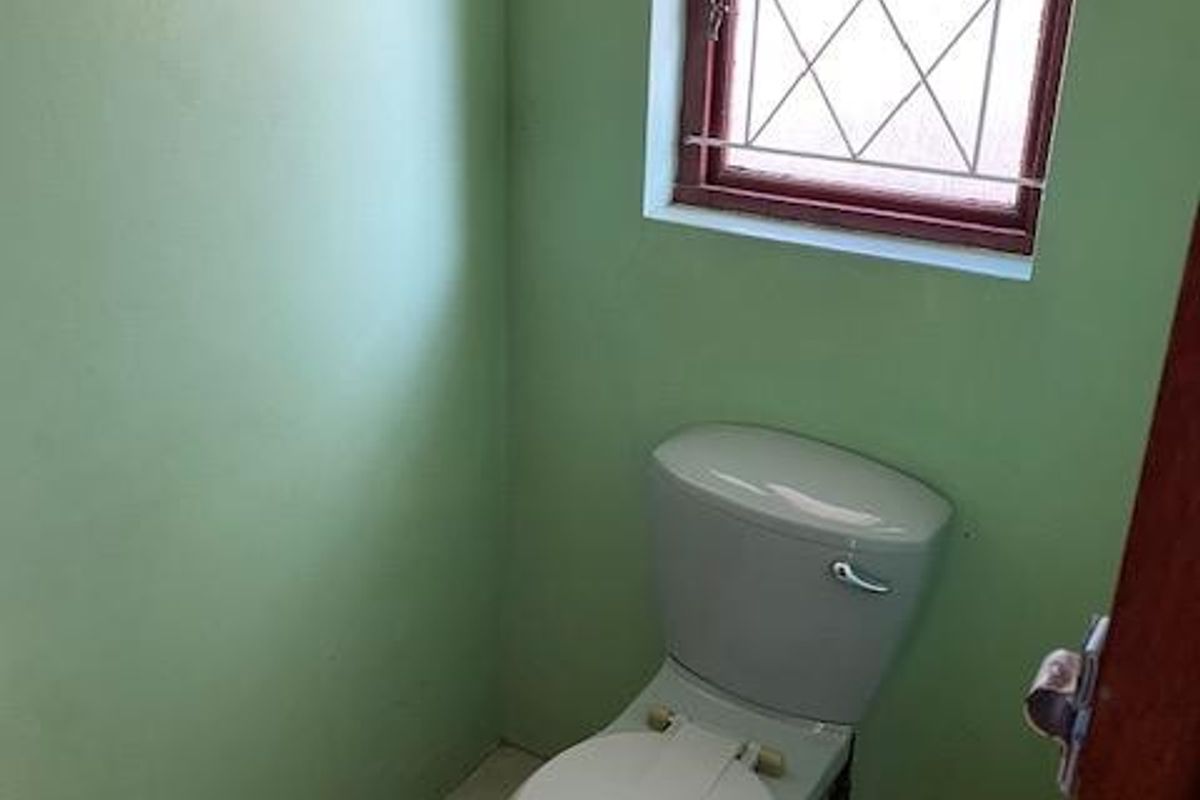 A small, functional bathroom featuring a standard toilet, tiled flooring, and a window with security bars.