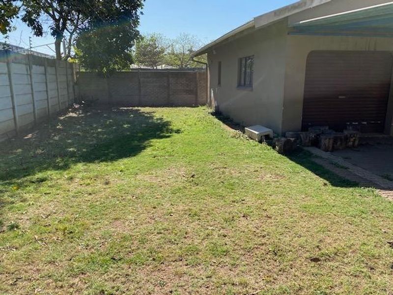 A view of the rear yard featuring a grass lawn, precast concrete boundary wall, and the side elevation of the garage with a roller door.