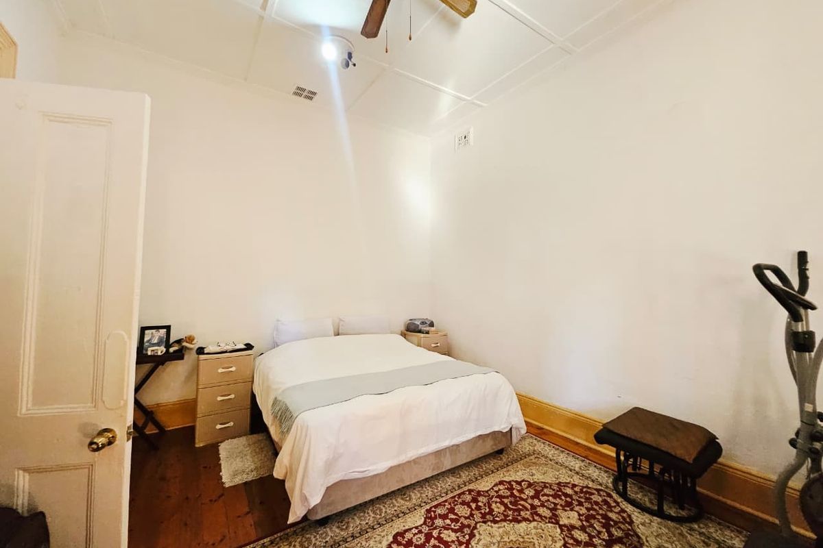 A bedroom featuring timber flooring, a ceiling fan, and classic skirting boards, providing a functional space with potential for cosmetic updates.