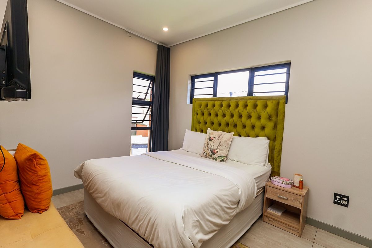 A well-maintained bedroom featuring neutral walls, tiled flooring, and aluminium-framed windows, providing a clean and functional living space.