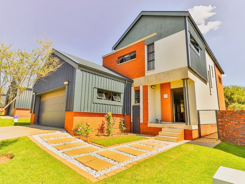 Modern double-story residential home featuring a combination of brick and metal cladding, an integrated garage, and a well-maintained front garden with paved walkway.