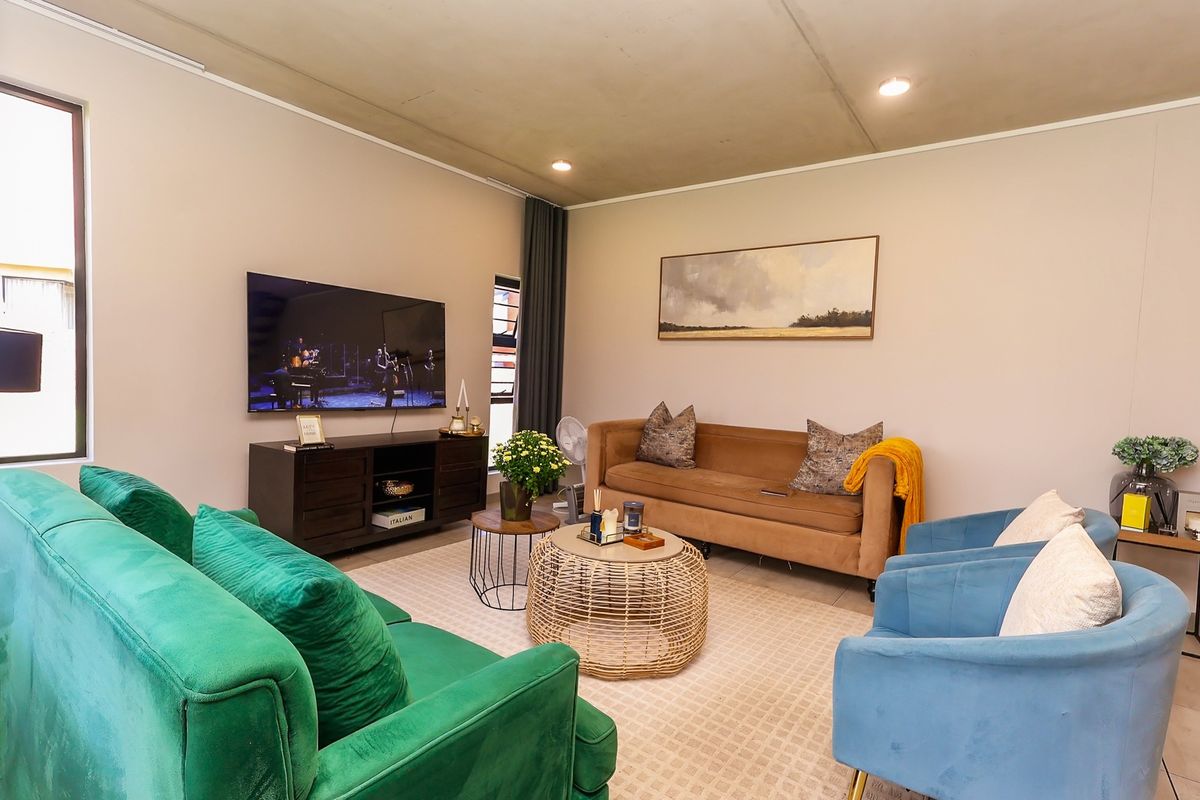 A modern living room featuring an exposed concrete ceiling, recessed downlighting, and large windows with aluminium frames.