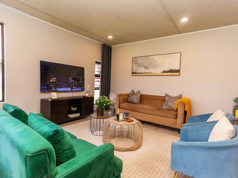 A modern living room featuring an exposed concrete ceiling, recessed downlighting, and large windows with aluminium frames.