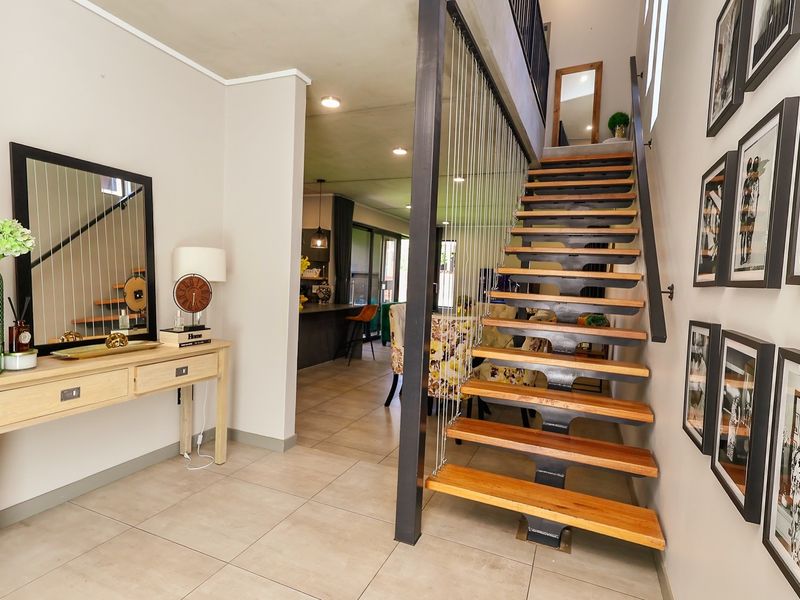 Modern entrance hallway featuring an open-tread staircase with steel cable balustrades and neutral tiled flooring, leading into an open-plan living area.
