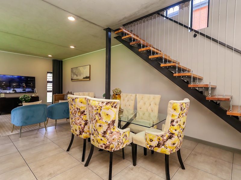 Open-plan living and dining area featuring modern tiled floors, recessed lighting, and a striking staircase with timber treads and steel cable balustrades.