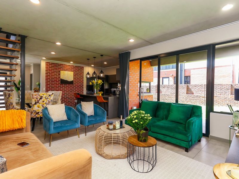 Spacious open-plan living and kitchen area featuring an exposed brick wall, modern staircase, and large sliding doors leading to an outdoor patio.