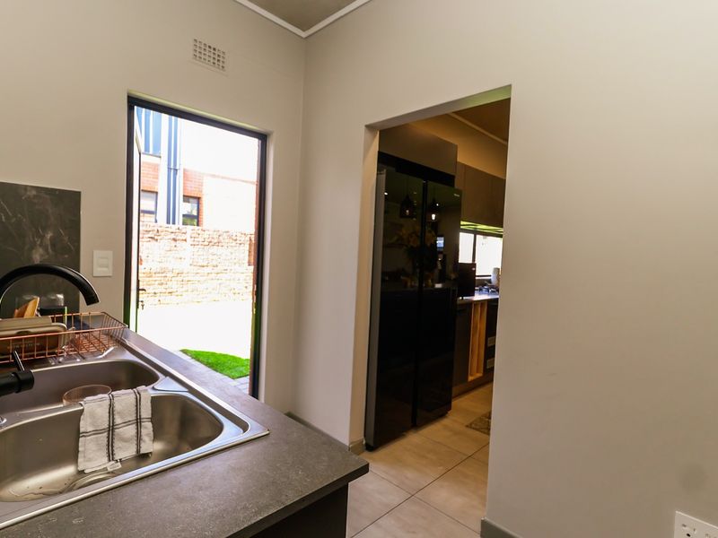 A clean and functional scullery area featuring a double bowl sink, modern black tapware, and direct access to the rear exterior.