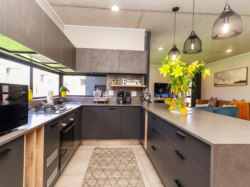 Modern open-plan kitchen featuring dark matte cabinetry, stone countertops, a central island, and integrated appliances, flowing seamlessly into the adjacent living area.