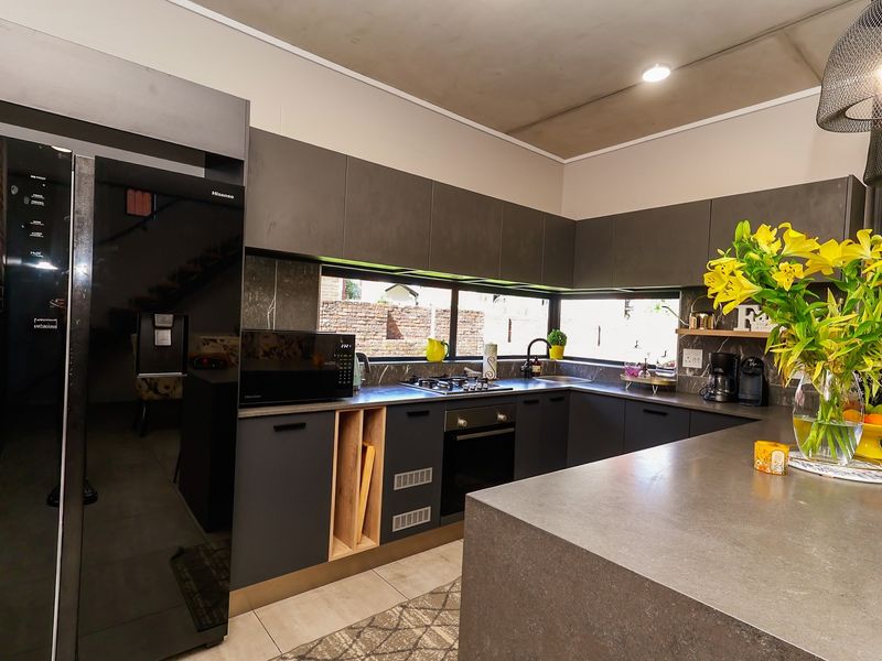 Modern kitchen featuring dark cabinetry, stone countertops, a central island, and integrated appliances, offering a sleek and functional culinary space.