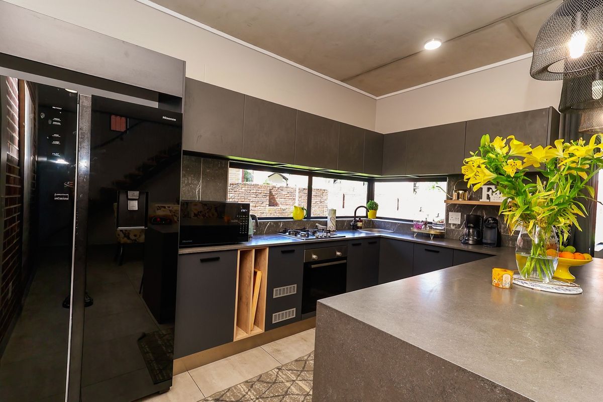 Modern kitchen featuring dark cabinetry, stone countertops, a central island, and integrated appliances, offering a sleek and functional culinary space.