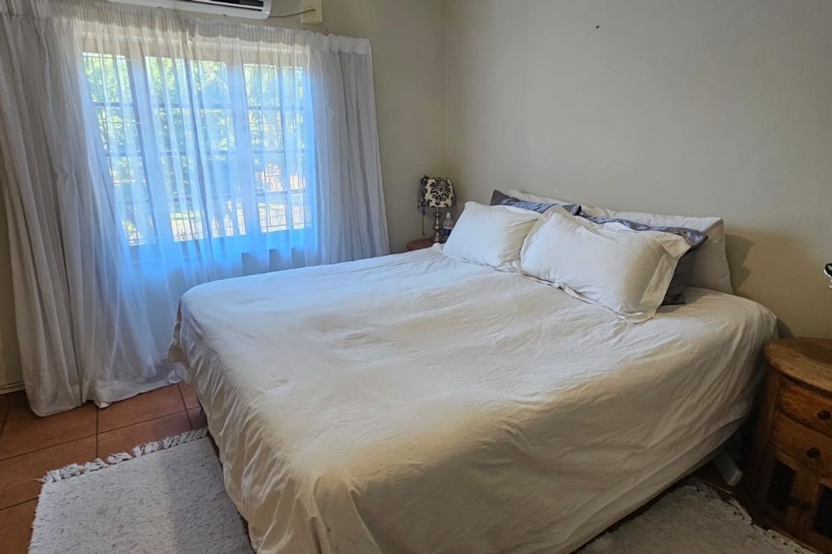 A standard bedroom featuring tiled flooring, a wall-mounted air conditioning unit, and a window with curtain fixtures.