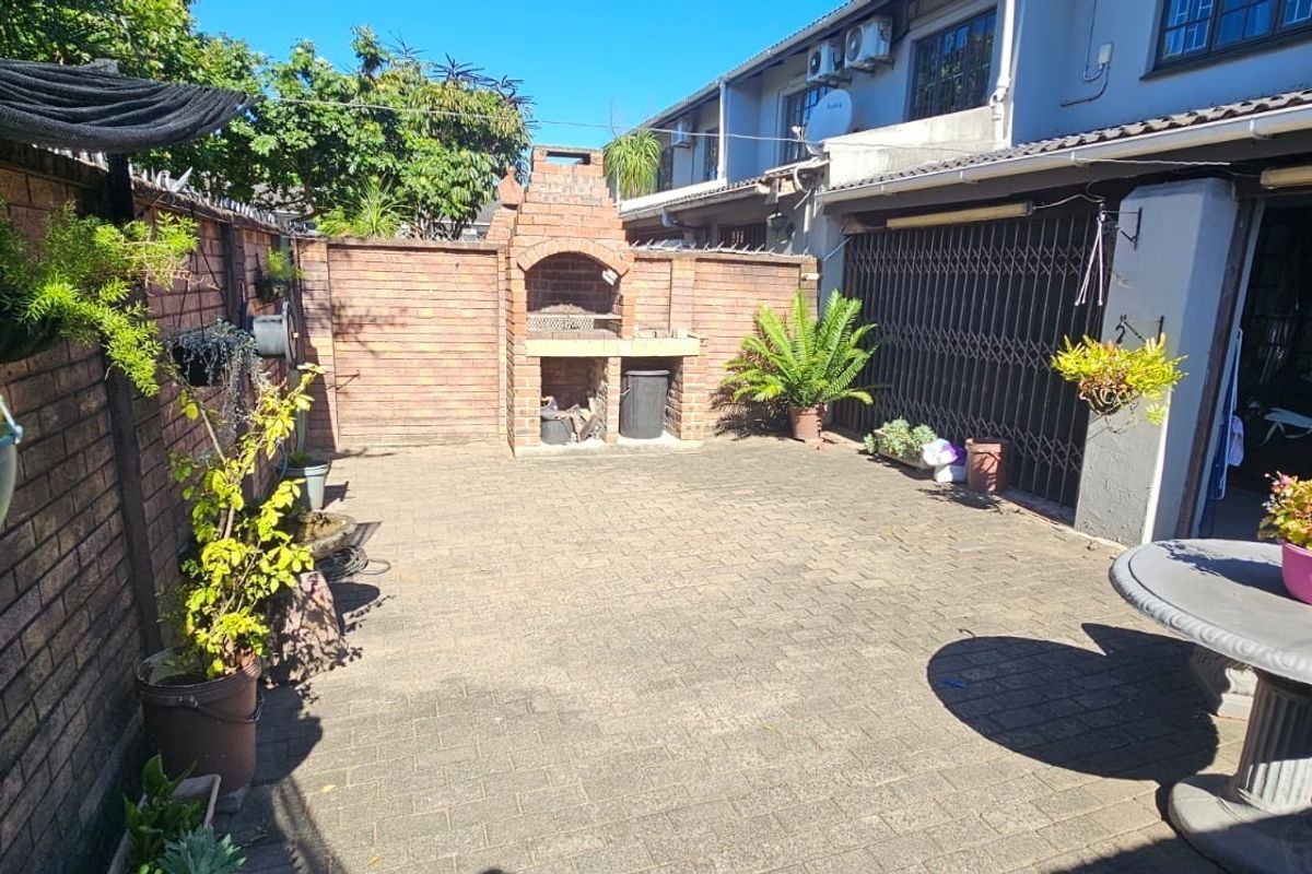 A paved rear courtyard featuring a built-in brick braai area, enclosed by perimeter brick walls and providing access to the townhouse interior.