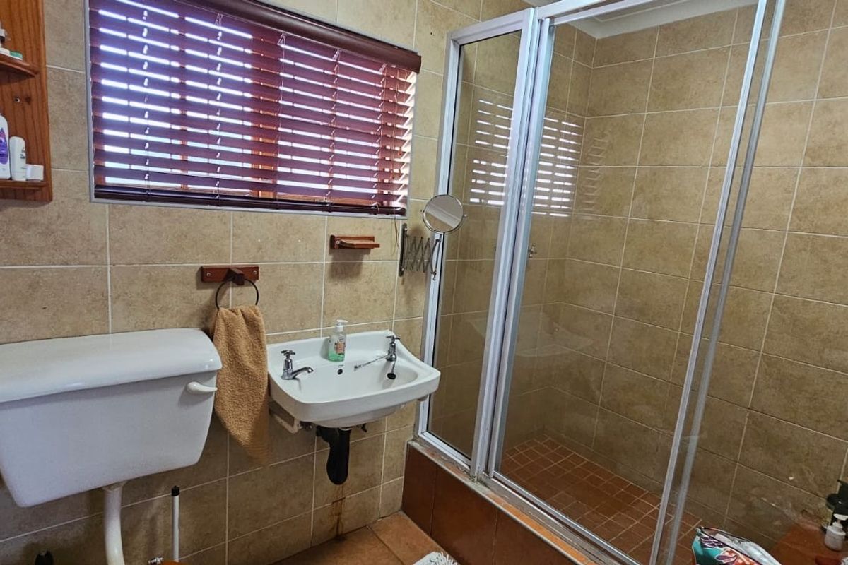 A functional bathroom featuring a shower enclosure with a glass door, wall-mounted basin, and toilet, finished with neutral wall and floor tiling.