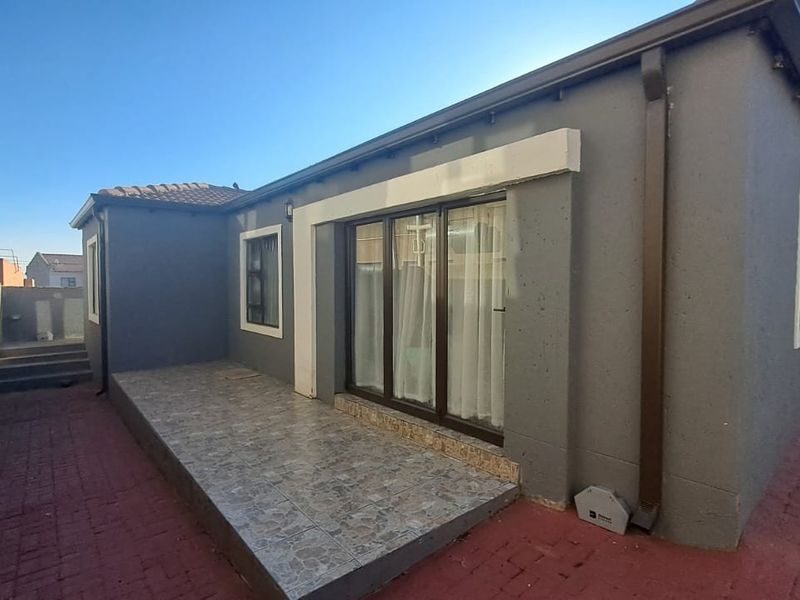 Rear view of the property featuring a paved patio area, sliding glass doors, and exterior wall finishes.