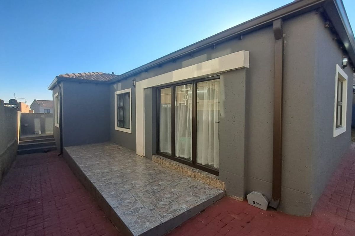 Rear view of the property featuring a paved patio area, sliding glass doors, and exterior wall finishes.